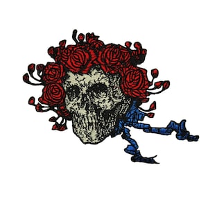 May include: An embroidered patch featuring a skull with red roses and a blue ribbon. The skull is surrounded by red roses and has a blue ribbon tied around it.