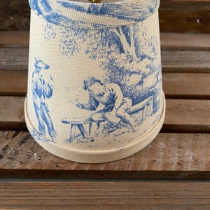 May include: A white lampshade with a blue and white toile pattern featuring a scene of two figures in a garden setting.