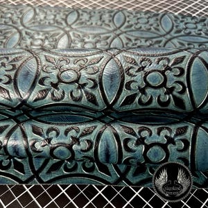 May include: A piece of teal and black embossed leather featuring a repeating geometric pattern of circles and stylized floral motifs. The surface has a textured finish with deep black lines defining the intricate shapes. A circular logo is visible.