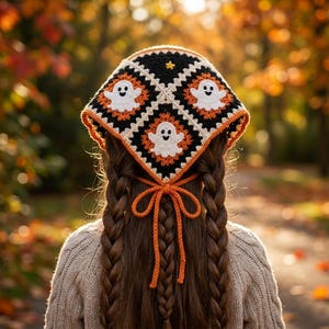 May include: A triangular crochet headscarf featuring a granny square pattern with black, white, and orange yarn. The design includes white ghost motifs on black squares and is secured at the back with orange crochet ties.