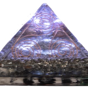 May include: A translucent purple pyramid-shaped object featuring embedded copper wire coils arranged in a spiral pattern. The base contains a layer of dark metallic shavings encased within the clear resin material, creating a layered visual effect.