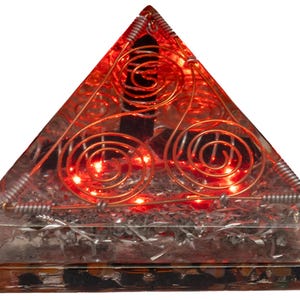May include: A pyramid-shaped resin object containing embedded copper wire spirals and silver-colored metallic shavings. The interior is illuminated by small red LED lights, and a dark, vertical crystal-like element is visible near the apex.
