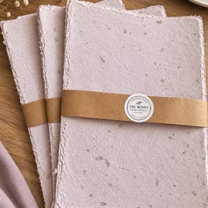 May include: A stack of three rectangular sheets of light lavender handmade paper with deckled edges and visible fibre inclusions. The stack is secured with a brown paper band featuring a circular white sticker that reads The Wonky Paper Company.