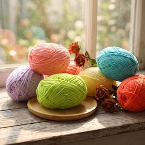 May include: A collection of seven round balls of thick, soft yarn in pastel and vibrant colors including light purple, peach, lime green, yellow, turquoise, and orange, arranged on a round wooden tray with small brown decorative flowers.