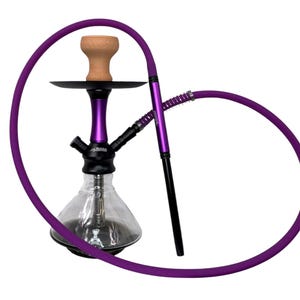 May include: A hookah with a clear glass base, a black and purple metal stem, and a tan clay bowl. A long, flexible purple hose is attached, featuring a matching purple and black metal handle. The base of the stem displays the brand name Tiara.
