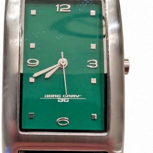 May include: A rectangular wristwatch with a brushed silver-tone metal case and a vibrant green dial. The face features silver-tone hour markers, Arabic numerals at 12, 3, 6, and 9, and the text Jorg Gray JG. It includes a black leather strap.