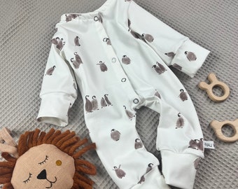 Könnte beinhalten: Weißer Baby-Strampler mit Pinguin-Druck. Der Strampler hat lange Ärmel und Druckknöpfe am Beinabschluss.