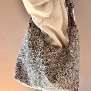 Könnte beinhalten: Eine große Tragetasche mit einem schwarz-weißen Leopardenmuster. Die Tasche ist aus Stoff gefertigt und hat einen breiten Schulterriemen. Die Tasche wird über der Schulter einer Person getragen.