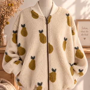 Könnte beinhalten: Eine cremefarbene, langärmelige Bomberjacke mit Reißverschluss aus strukturiertem Fleece-Material. Die Jacke ist mit einem durchgehenden Muster aus kleinen, dunkel olivgrünen birnenförmigen Motiven mit schwarzen Stielen sowie gerippten Bündchen versehen.
