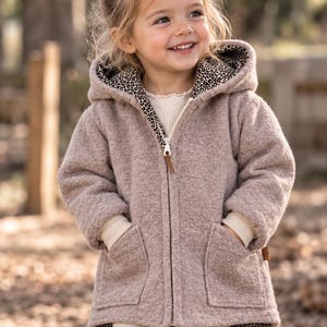 May include: A beige hooded jacket with a textured finish, featuring a front zip closure with a brown pull tab, two front patch pockets, and a black and white leopard print lining visible on the hood and along the inner hem edges.