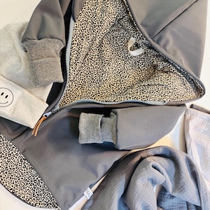 Könnte beinhalten: Eine graue Kapuzenjacke mit Leopardenmuster-Futter. Die Jacke hat einen Reißverschluss und ein kleines Etikett mit der Aufschrift "Fral" unten rechts.