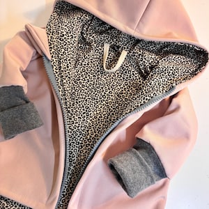 Op de afbeelding: Een roze hoodie met een luipaardprint voering. De hoodie heeft grijze manchetten en een ritssluiting. Het label "FRAU" is zichtbaar in de rechter benedenhoek.