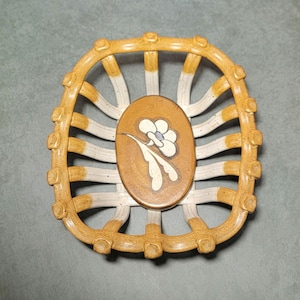 May include: A square ceramic basket with a lattice-style rim featuring a mustard yellow and off-white glaze. The center base is an oval medallion in a solid mustard brown tone, decorated with a hand-painted white flower with a light blue center.