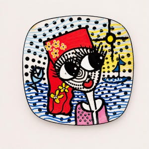 Peut inclure: Une assiette carrée en céramique présentant une illustration stylisée d'une personne aux grands yeux, portant un foulard rouge à fleurs jaunes. Le fond comprend des pois noirs, des lignes ondulées bleues, un soleil jaune, un voilier et un poisson.
