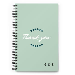 May include: A light sage green spiral-bound notebook featuring the white text Thank you centred between two dark teal leaf-shaped decorative flourishes. The bottom right corner displays the black letters C & S in a simple serif font.