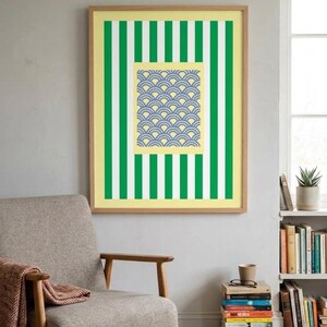 Puede incluir: Una impresión de arte mural rectangular enmarcada que presenta un patrón vertical de rayas alternas verdes y blancas sobre un fondo amarillo pálido, con un bloque cuadrado central que contiene un diseño repetitivo de ondas arqueadas azules y blancas.