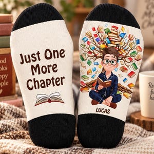 Può includere: Un paio di calzini color crema con polsini neri. Il calzino sinistro presenta il testo "Just One More Chapter" sopra un libro aperto. Il destro mostra un personaggio dei cartoni che legge sotto un albero di libri con il nome "LUCAS".