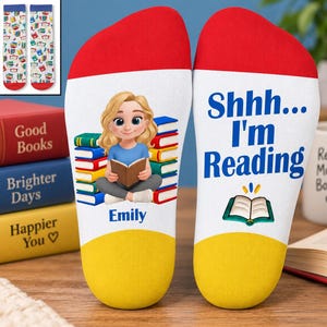 May include: A pair of white socks with red toes and yellow heels. One sock features a cartoon of a blonde person reading a book in front of a stack of books with the name Emily below. The other sock displays the text Shhh... I'm Reading and a book icon.
