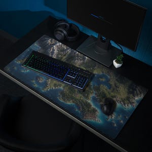 May include: A large rectangular desk mat featuring a detailed aerial map print of a coastal landscape with islands, forests, and blue water. The mat is placed on a black desk surface under a black computer keyboard, a black mouse, and headphones.
