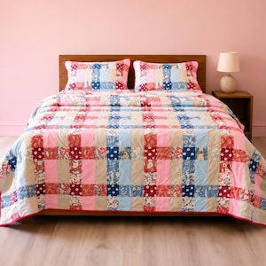 May include: A quilt and two matching pillow shams featuring a woven-look pattern of alternating solid pink, light blue, and beige fabric strips intersected by squares of red, blue, and white floral print fabric, covering a bed frame.