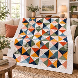 Op de afbeelding: Een rechthoekige quilt met een patchworkontwerp van driehoeken in diverse kleuren, waaronder marineblauw, mosterdgeel, saliegroen, koraal en wit. De stoffen bevatten kleine bloemenprints, ruitjespatronen en effen kleuren.
