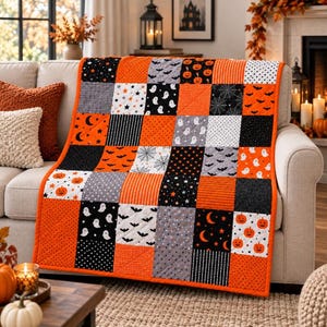 Może przedstawiać: Pikowana narzuta typu patchwork z siatką kwadratów o wzorach związanych z Halloween w kolorach pomarańczowym, czarnym, białym i szarym. Kwadraty z tkaniny przedstawiają motywy dyń, duchów, nietoperzy, pajęczyn, gwiazd, księżyców i kropek.