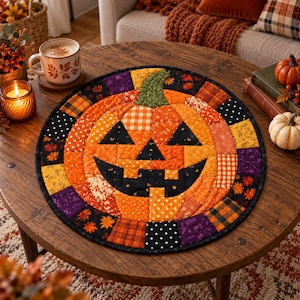 Può includere: Un tappetino rotondo in tessuto trapuntato con un design centrale a forma di zucca di Halloween composto da toppe di tessuto arancione, giallo e nero. Il bordo è costituito da vari quadrati fantasia nei toni del viola, arancione, nero e giallo con motivi a foglie e pois.