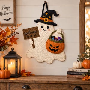 May include: A quilted wall hanging shaped like a white ghost wearing a black witch hat with yellow stars. The ghost holds a brown wooden sign that says welcome and carries an orange jack-o'-lantern bucket filled with small candy wrappers.