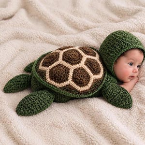 Puede incluir: Un disfraz de tortuga de ganchillo que consiste en una pieza de color verde oscuro con capucha, aletas adjuntas y un caparazón texturizado. El caparazón presenta un centro marrón oscuro con un borde crema, creando un patrón hexagonal.