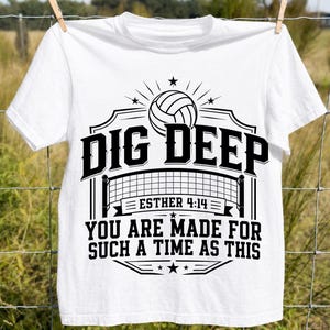 Op de afbeelding: Een wit t-shirt met korte mouwen en een zwarte grafische print van een volleybal boven een net. De tekst luidt DIG DEEP, ESTHER 4:14 en YOU ARE MADE FOR SUCH A TIME AS THIS, geplaatst in een decoratief kader met sterren en lijnen.