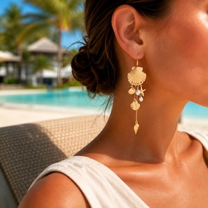May include: A gold-toned dangle earring featuring a large fan-shaped shell at the top, followed by a delicate chain adorned with smaller shell charms, a starfish charm, and two small white pearls, creating a layered, multi-charm drop design.