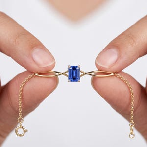 Pode incluir: Uma pulseira de corrente dourada com uma safira azul central de corte esmeralda. A pedra está fixada numa cravação de quatro garras, ladeada por dois elos dourados simétricos e vazados que se ligam a uma corrente fina com fecho de mola.