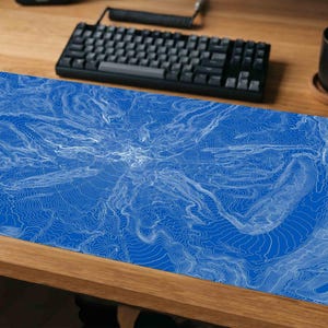 May include: A rectangular desk mat featuring a vibrant blue background with intricate, thin white topographic contour lines that radiate outward from the center, creating a detailed map-like pattern across the entire surface area.