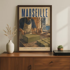May include: A framed vintage-style poster titled MARSEILLE featuring an illustration of a person in an apron using a wire cutter on a large green soap block. The text at the bottom reads CUTTING THE FIRST SOAP BLOCK. The poster is in a dark brown frame.