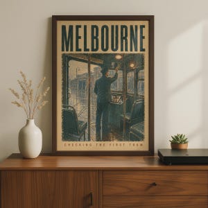 May include: A framed rectangular poster titled MELBOURNE with the subtitle CHECKING THE FIRST TRAM. The artwork depicts a person in a dark uniform standing inside a tram cabin, looking out at a rainy street scene through the large front windows.