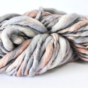 May include: A skein of chunky yarn in shades of gray, white, and peach. The yarn is soft and fluffy, and it would be perfect for knitting or crocheting a cozy blanket or sweater.