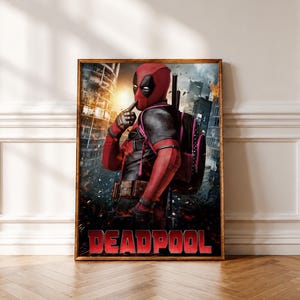 Op de afbeelding: Een ingelijste poster met het personage Deadpool in een rood en zwart pak met een zwarte rugzak, die een vinger naar het masker houdt in een stiltegebaar. De achtergrond toont een stad in puin met vuur en rook. Het woord DEADPOOL is in het rood.