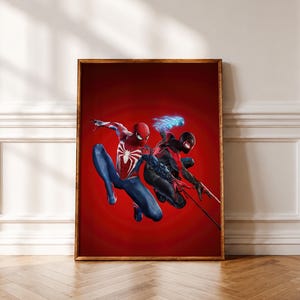 Op de afbeelding: Een ingelijste kunstdruk met twee figuren in superheldenkostuums tegen een effen rode achtergrond. Eén figuur draagt een rood-blauw pak met een wit spinnenembleem, de andere een zwart-rood pak met blauwe energie-effecten.