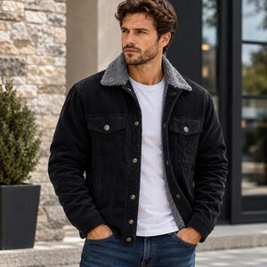 May include: A black corduroy jacket featuring a grey sherpa collar and lining, a button-front closure, and two chest pockets with buttoned flaps. The jacket is worn over a plain white t-shirt and paired with blue denim jeans for a layered look.
