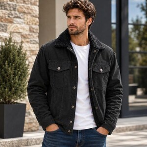 May include: A black denim jacket featuring a dark textured sherpa collar and lining, a button-up front with metallic buttons, two chest pockets with buttoned flaps, and long sleeves, worn over a plain white t-shirt and blue denim jeans.