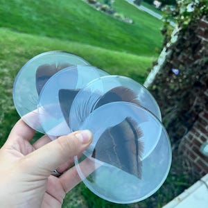 Op de afbeelding: Een set van vier ronde, transparante acryl onderzetters, elk met een bruine en zwarte kalkoenveer ingebed in het heldere materiaal. De onderzetters hebben gladde, afgeronde randen en een glanzende afwerking, waardoor de natuurlijke veerpatronen goed zichtbaar zijn.