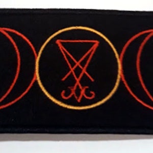 Könnte beinhalten: Ein schwarzer Patch mit einem roten und gelben gestickten Design. Das Design zeigt einen Kreis mit einem roten umgekehrten Pentagramm im Inneren, umgeben von zwei roten Halbmonden.