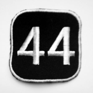 Puede incluir: Parche bordado en blanco y negro con el número 44 en blanco sobre un fondo negro.
