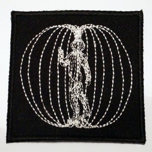 May include: White embroidered patch on a black background. The design features a stylized human figure inside a circle of lines.