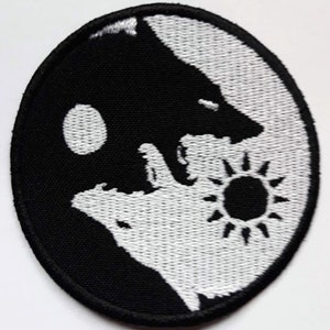 Op de afbeelding: Zwart-witte geborduurde patch met een yin yang symbool met een wolf aan elke kant. De wolf aan de linkerkant kijkt naar rechts en de wolf aan de rechterkant kijkt naar links. Het yin yang symbool is omgeven door een witte omtrek.