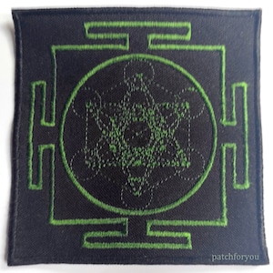 Può includere: Toppa ricamata verde con un design geometrico su sfondo nero. Il design presenta un quadrato con un cerchio all'interno e un motivo complesso di linee e forme all'interno del cerchio.