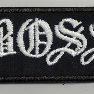 Pode incluir: Patch retangular preto com o texto "BOSS" bordado em branco.