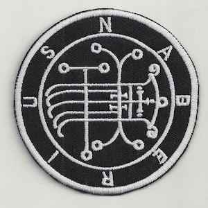 Op de afbeelding: Zwart-witte geborduurde patch met een cirkelvormig ontwerp. Het ontwerp heeft een complex geometrisch patroon met een kompasroos aan de buitenrand. De letters N, S, E en W zijn zichtbaar op de kompasroos.