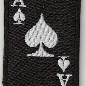 Może przedstawiać: Czarny materiałowy znaczek z haftowanym wzorem karty do gry w kolorze białym. Karta to As Pik. Kolor to pik, a liczba to A.