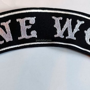 Op de afbeelding: Een geborduurde zwarte en witte patch met de tekst "LONE WOLF" in een wit cursief lettertype.